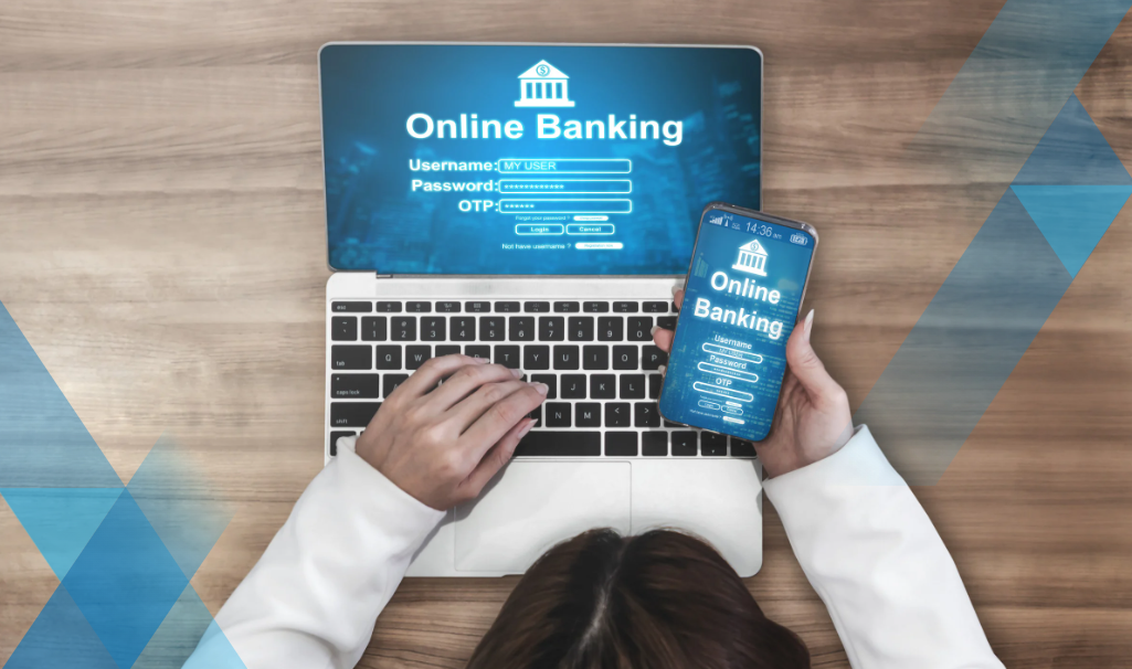 laptop on wood table with online banking site up, woman's hands on laptop and has mobile phone in hand with online banking site on screen