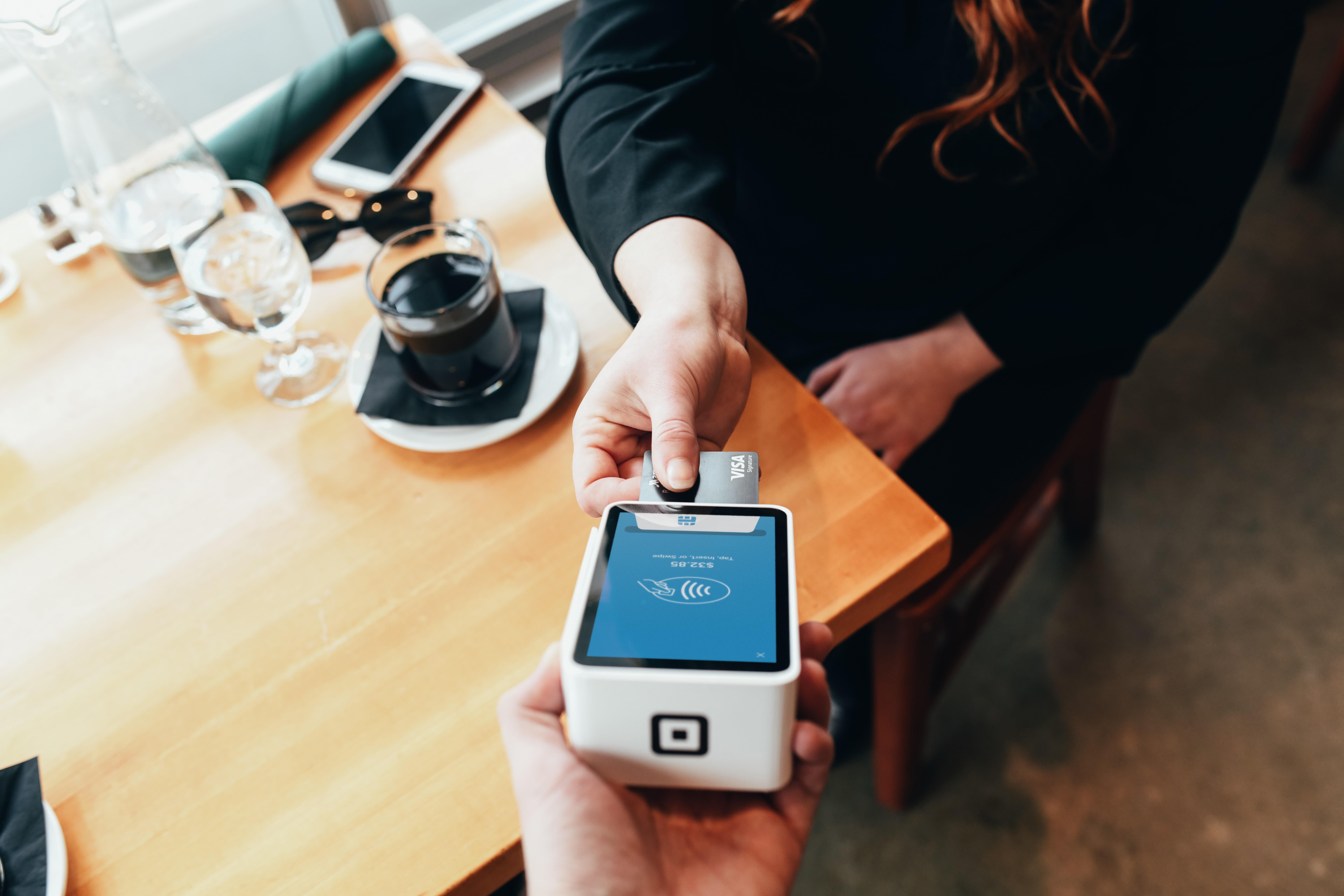 Women sitting at a table in a restraunt with beverages on the table. She is inserting her card into a card reader to pay for her items. 
